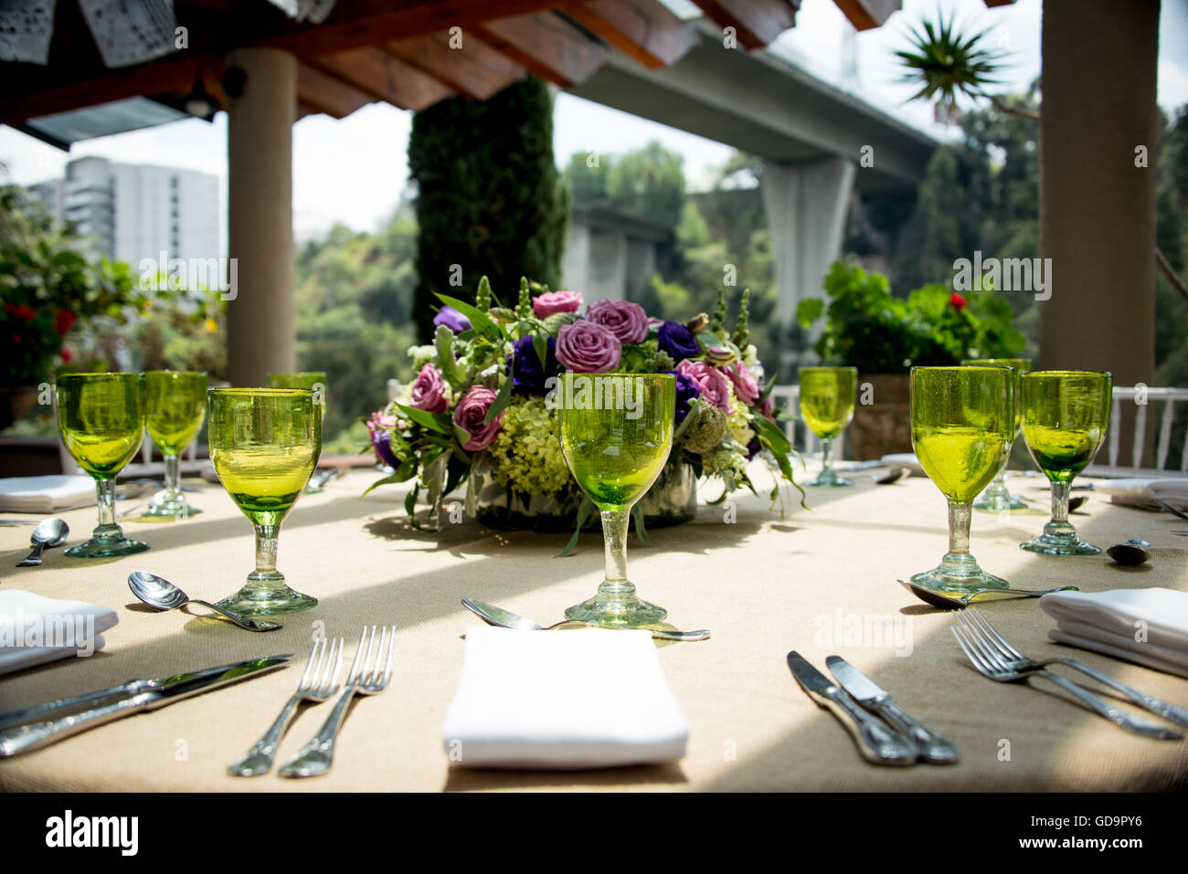 Elegante impostazione tabella per un open-air nozze con green wineglasses, argenteria e biancheria su una tabella su un soleggiato patio urbano Foto Stock