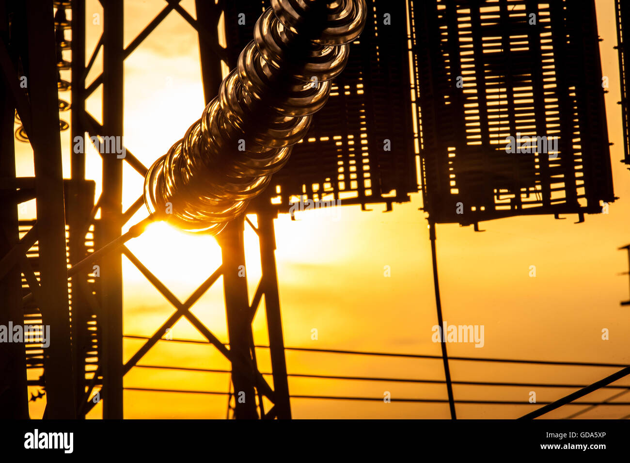 Le linee elettriche, poli e un isolatore di vetro in una stazione di alimentazione, al tramonto. Foto Stock