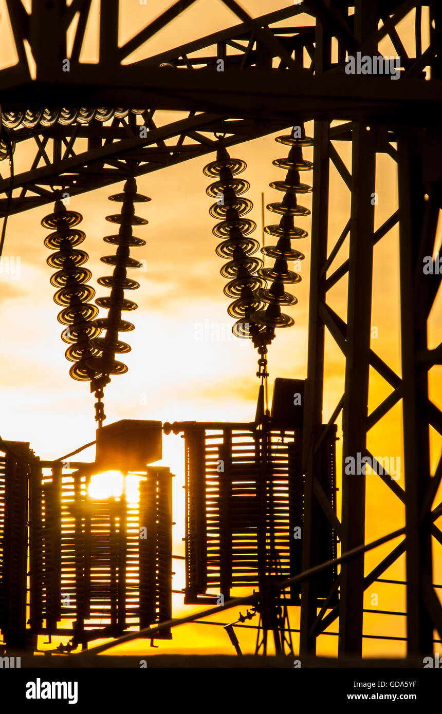 Le linee elettriche, i poli e gli isolatori di vetro in una stazione di alimentazione al tramonto Foto Stock