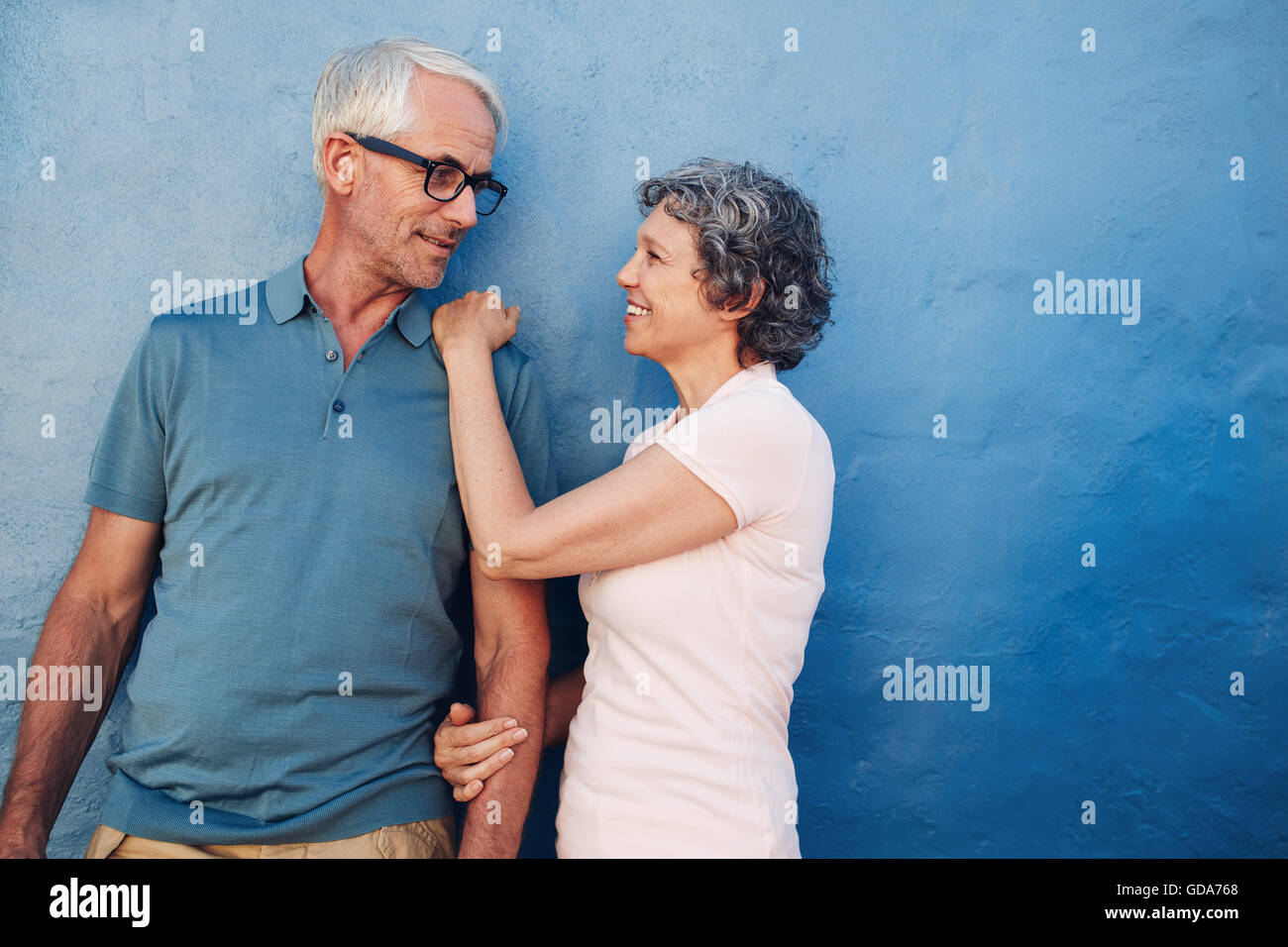 Ritratto di amare l uomo maturo e la donna guardando ogni altro. Coppia romantica in piedi insieme contro una parete di blu. Foto Stock