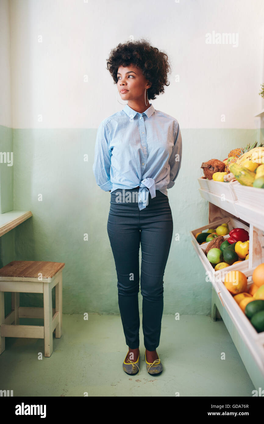 A piena lunghezza Ritratto di giovane donna africana in piedi in un juice bar e guardando lontano. Foto Stock
