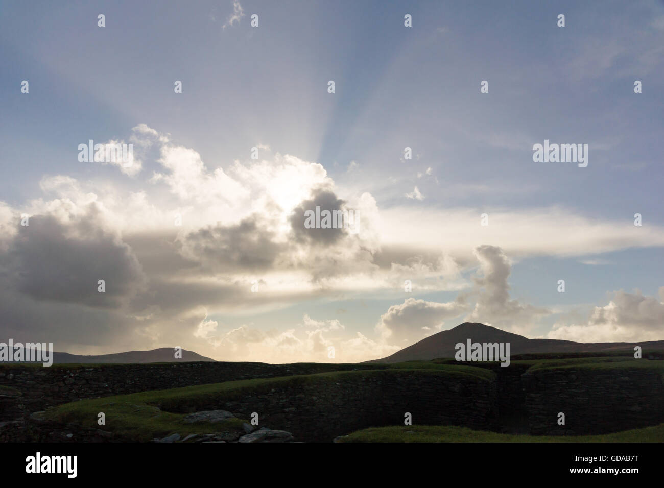 Irlanda, Kerry County Kerry, a pietra Leacanabuaile Fort, sun dietro una formazione delle nuvole in un paesaggio collinare Foto Stock