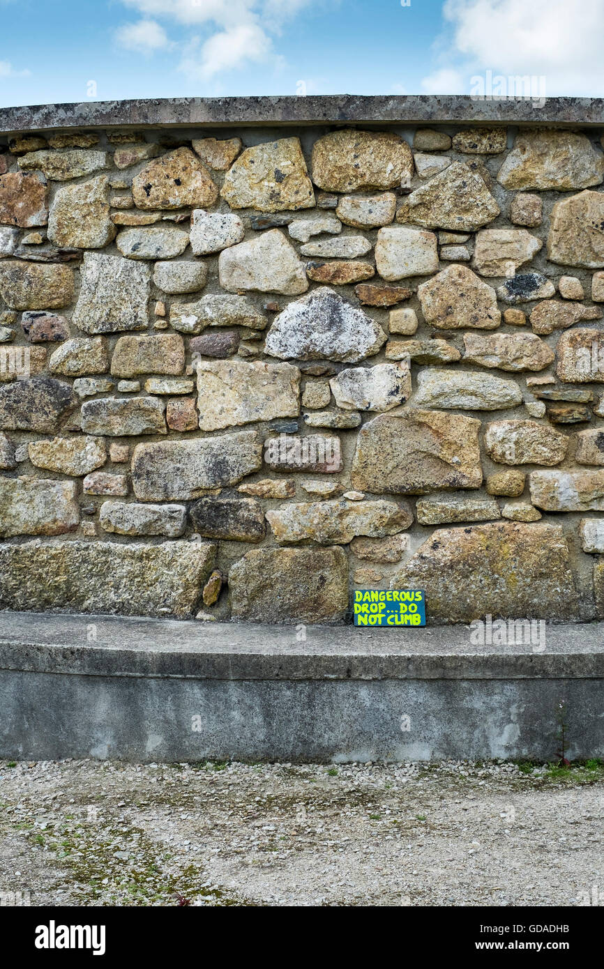 Un piccolo segno di avvertimento si appoggia contro un muro di pietra. Foto Stock