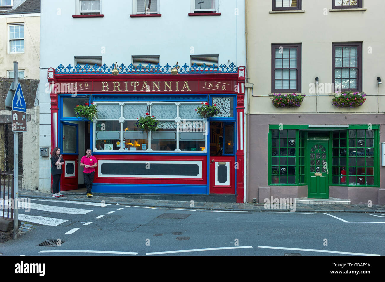 Pub Britannia in stile inglese tradizionale a St Peter Port, Guernsey con due persone per fumare all'aperto Foto Stock