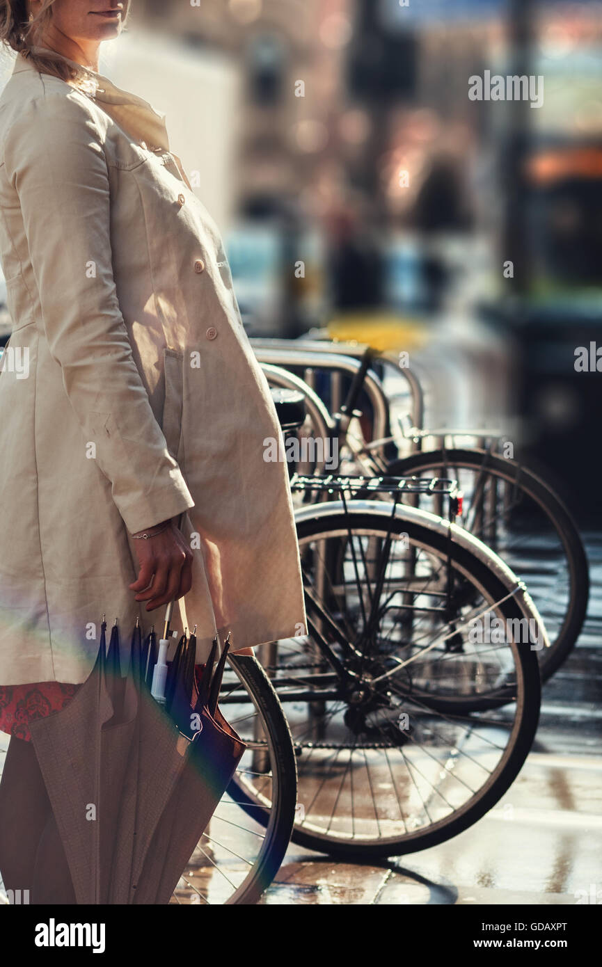 Giovane donna in piedi dalle biciclette con ombrellone Foto Stock