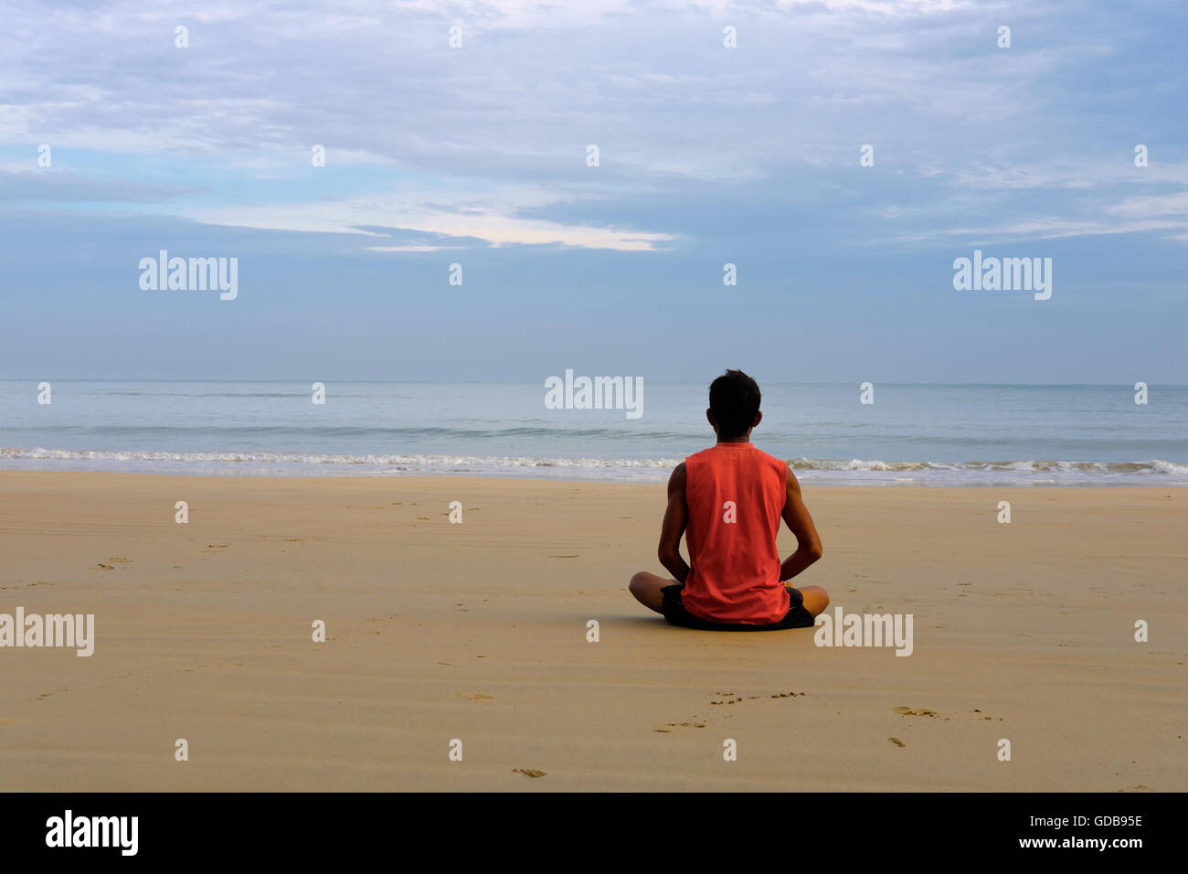 Giovane ragazzo tailandese in rosso t-short medita sulla spiaggia vicino al mare in Lotus Foto Stock