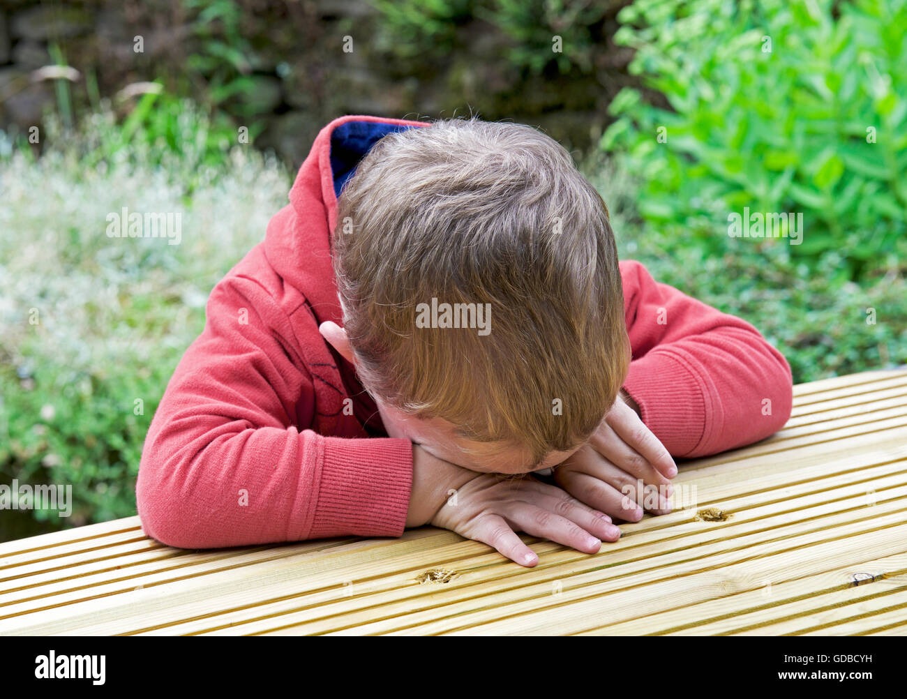 Il ragazzo, due anni, seduti a un tavolo e la sensazione di essere triste Foto Stock