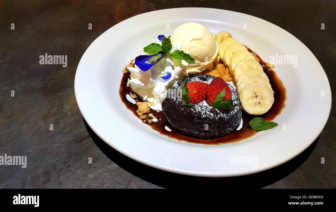 Il cioccolato fondente torta lavica decorata con spolverata di zucchero a velo, fragole fresche, banana e gelato Foto Stock