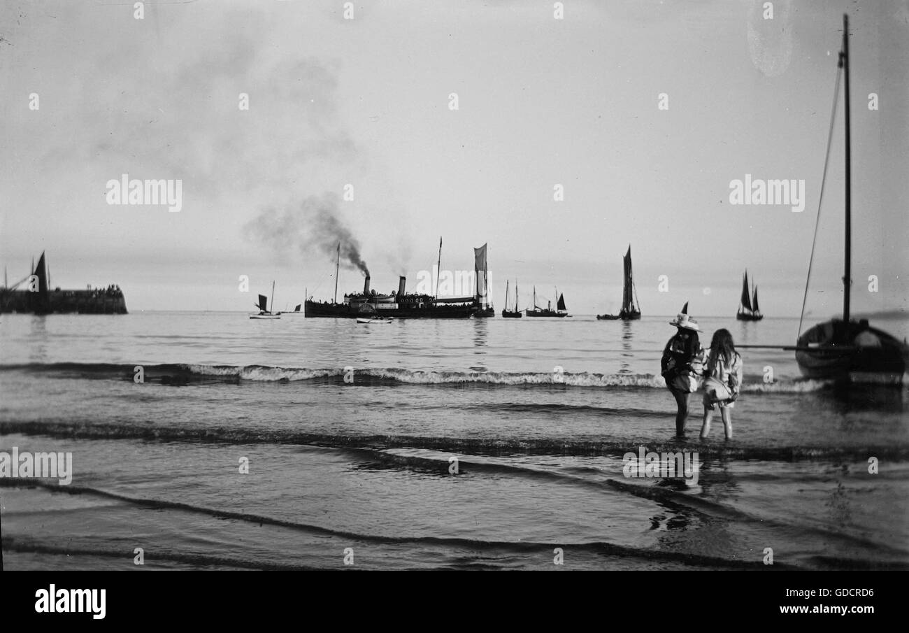 Meravigliosamente immagine atmosferica di due ragazze paddling in mare alla ricerca su come un vapore in barca a remi è pronta a salpare. c 1910. Fotografia di Tony Henshaw Foto Stock