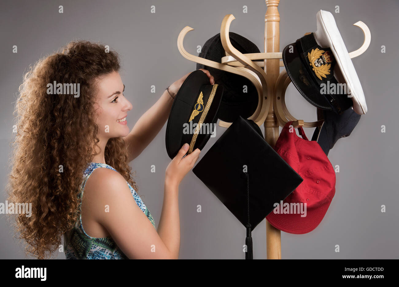 Giovane donna disponendo cappelli da una selezione delle professioni su un cappello di stand Foto Stock