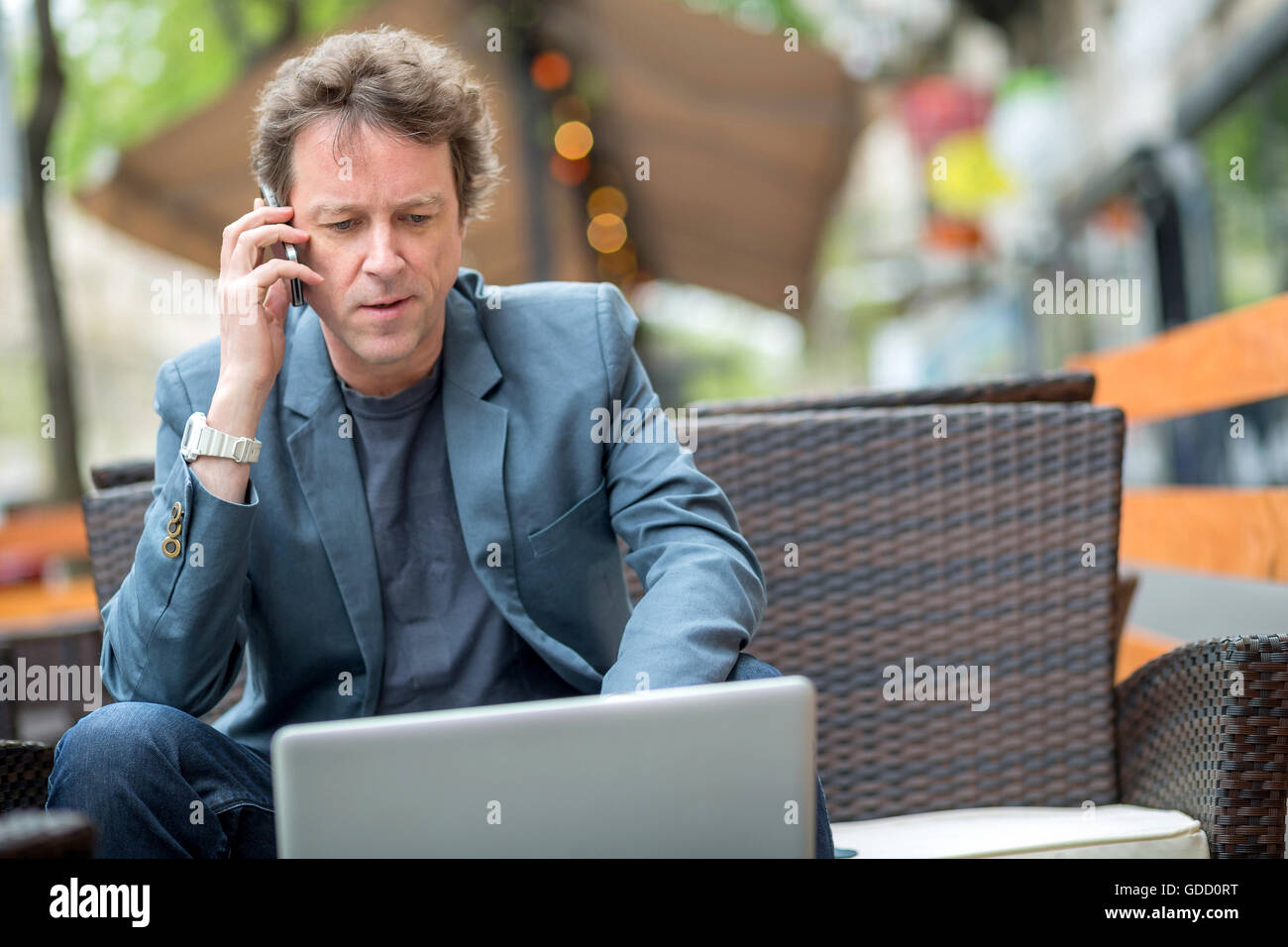 Ritratto di un medioevo imprenditore ubicazione sulla terrazza di un caffè e di parlare al telefono. Foto Stock