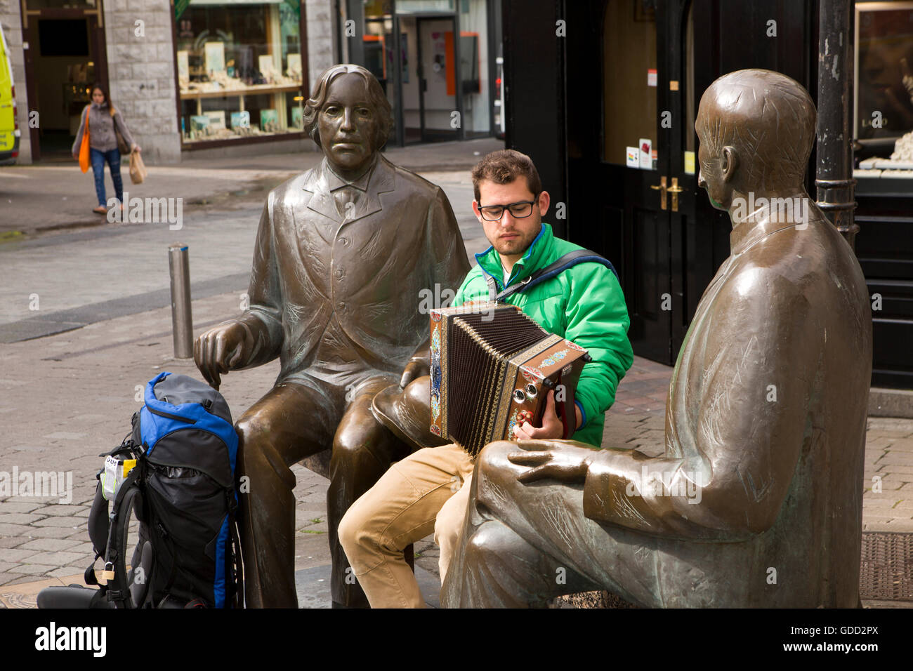 Irlanda, Co Galway, Galway, Shop Street, musicista di strada backpacker a suonare la fisarmonica su Oscar Wilde e Eduard Vilde statue Foto Stock