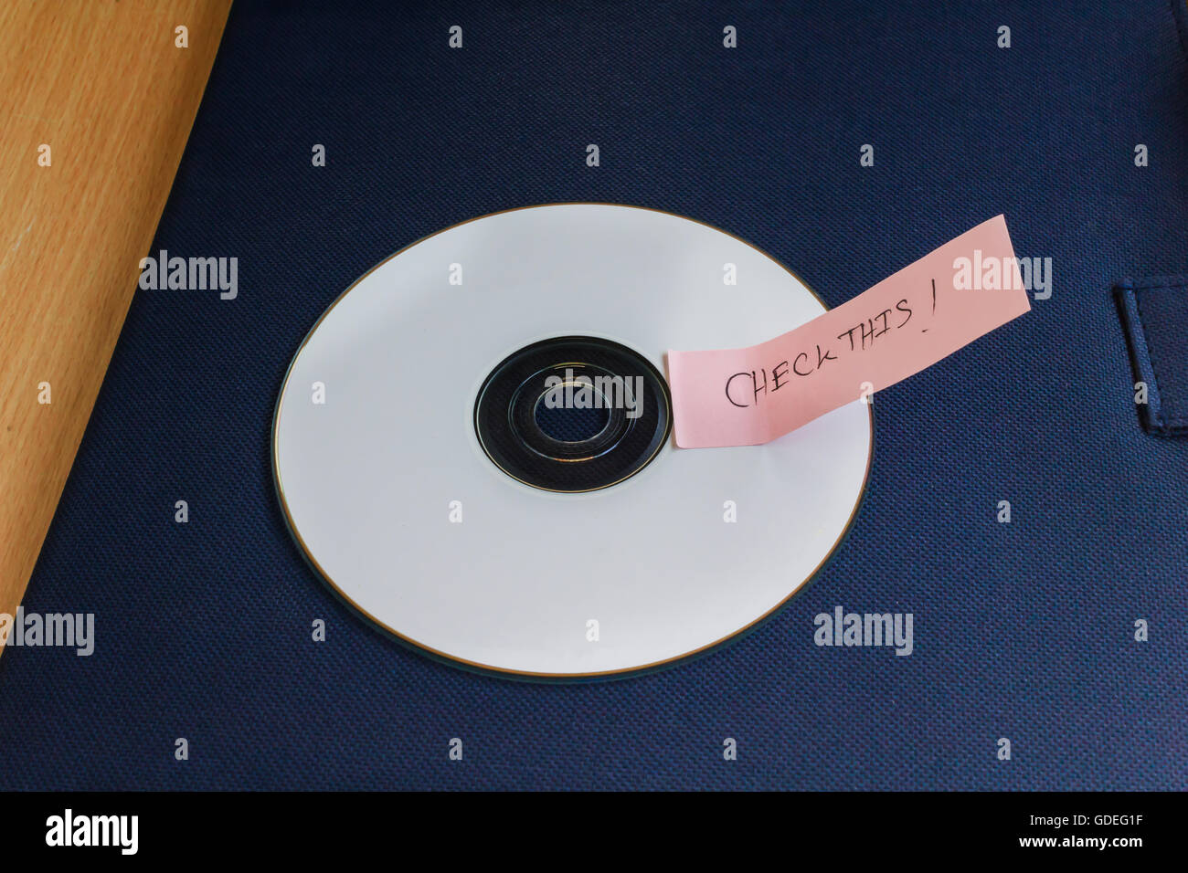 White CD o disco compatto con la nota di testo parola controllare questo sul blu scuro documento sul tavolo con spazio di copia Foto Stock