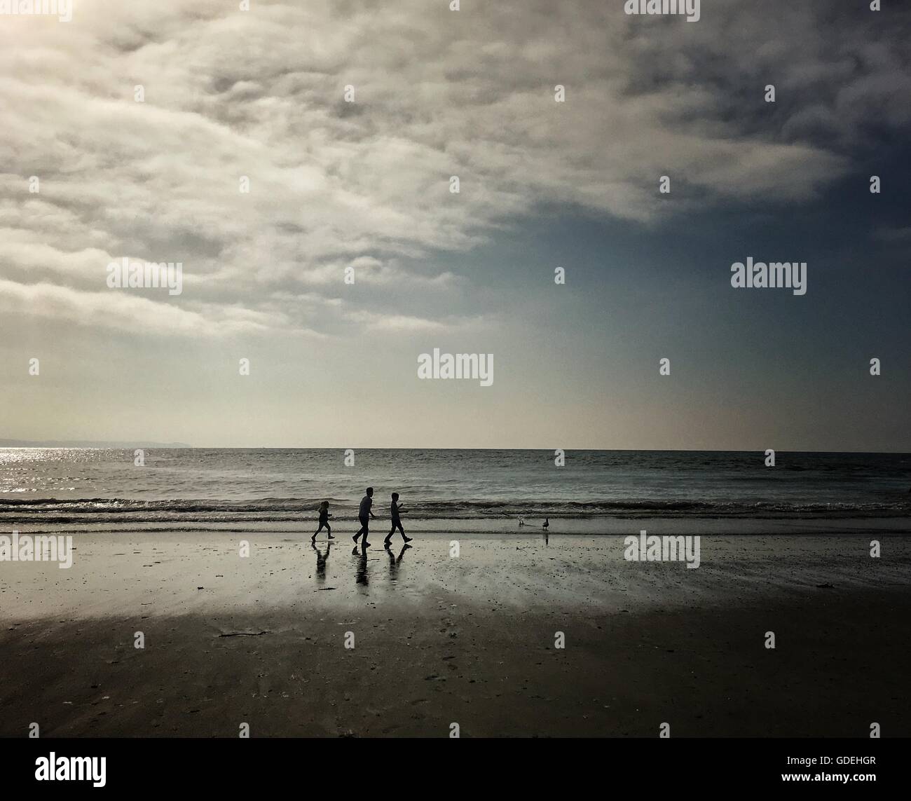 Silhouette di tre bambini passeggiate sulla spiaggia Foto Stock