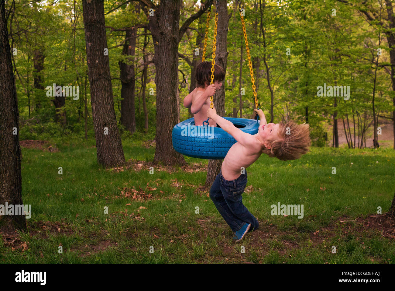 Due giovani ragazzi giocare su tire swing in foresta Foto Stock