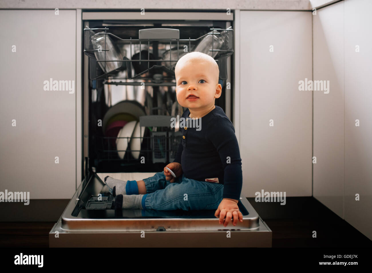 Bambino seduto su Aprire sportello di lavastoviglie Foto Stock