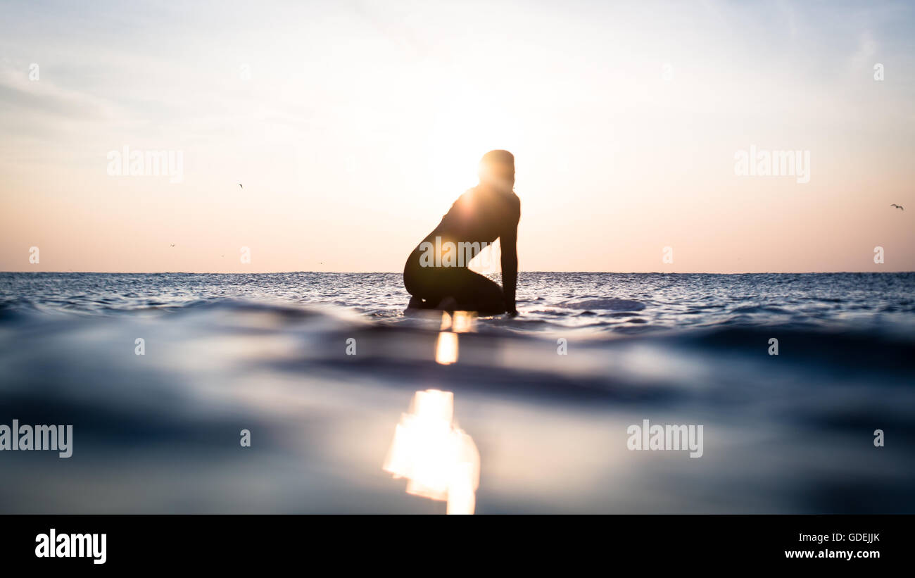 Silhouette di una donna seduta sulla tavola da surf in oceano, Malibu, California, america, STATI UNITI D'AMERICA Foto Stock