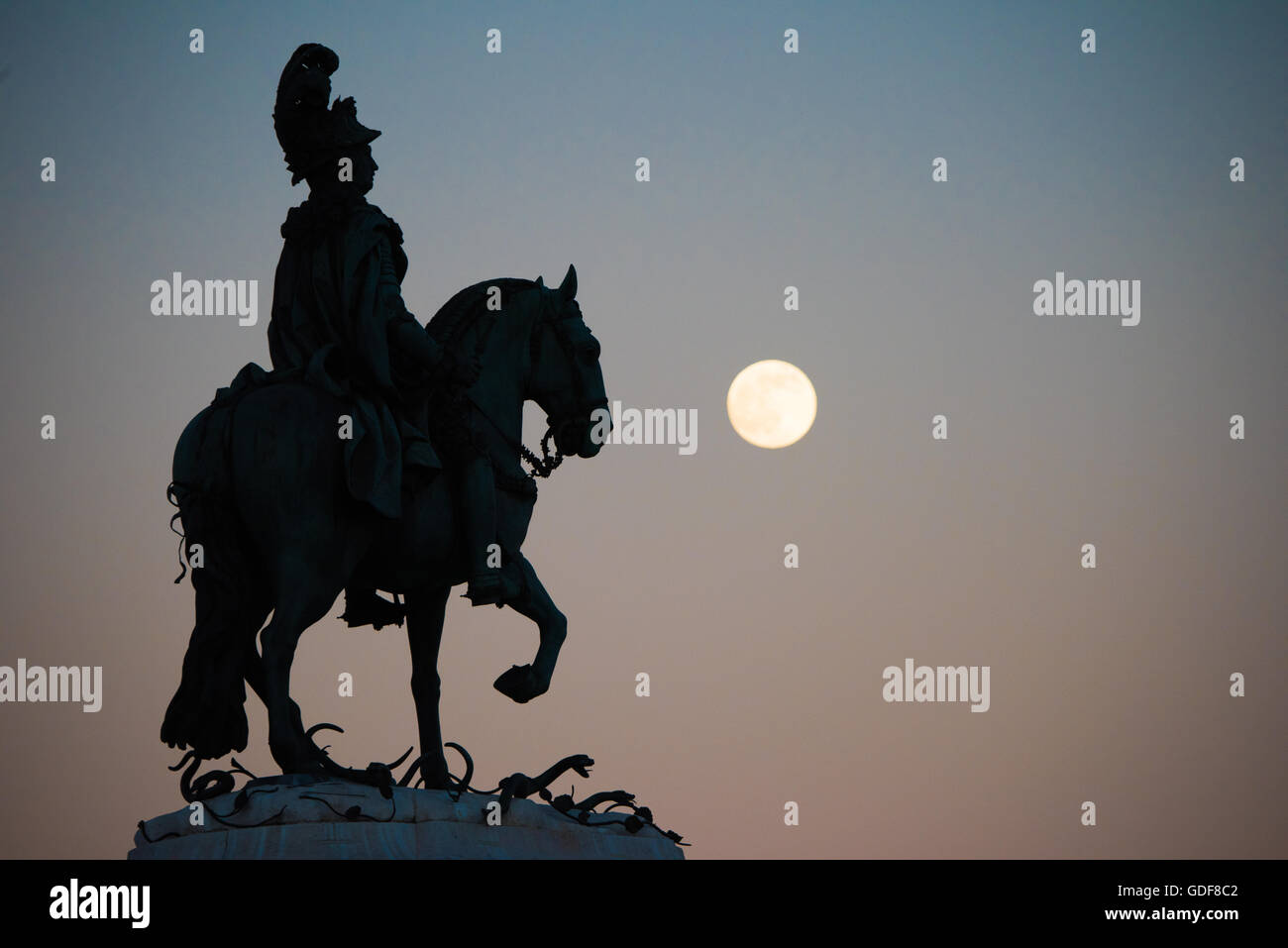 Statua equestre di re Giuseppe i Prac do Comércio Lisbona // LISBONA, Portogallo — la statua equestre di re Giuseppe i, creata dallo scultore Joaquim Machado de Castro, si trova in primo piano nel centro di Prac do Comércio (Piazza del commercio) nel quartiere Pombaline Downtown di Lisbona con una luna piena visibile sullo sfondo. Dietro la statua, è visibile la cima dell'Arco da Rua Augusta, coronata da sculture che rappresentano la Gloria che gratifica il Valor e il Genio. Questa piazza storica, situata accanto al fiume Tago, mostra elementi chiave del design urbano e scultura portoghese del XVIII secolo. Il fratello Foto Stock