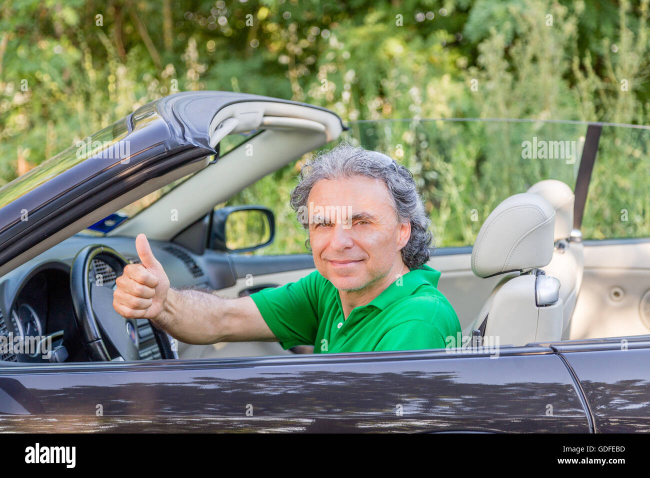 Uomo maturo alla guida di una vettura convertibile è felice e mostra la sua soddisfazione dalla sorridente e alza il pollice Foto Stock