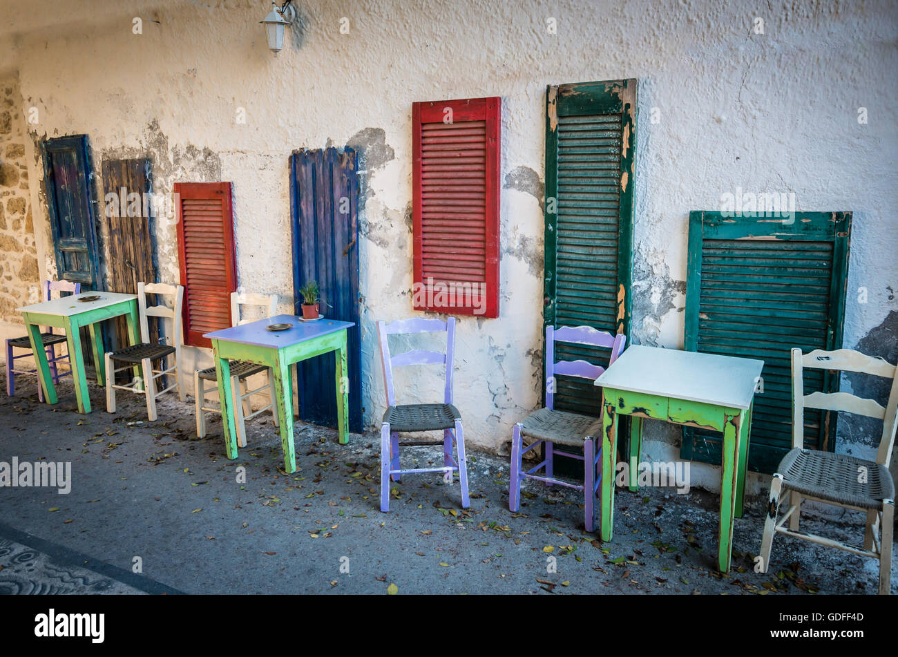 Vecchi tavoli e posti a sedere sulla strada. Verde e tavoli bianchi e bianco e viola sedi nei pressi di blu, verde e rosso di windows su una strada io Foto Stock