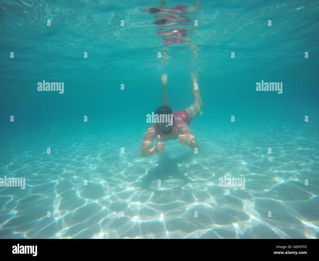 Barba giovane uomo in bicchieri con il pollice in alto le immersioni in acqua pulita azzurra Foto Stock