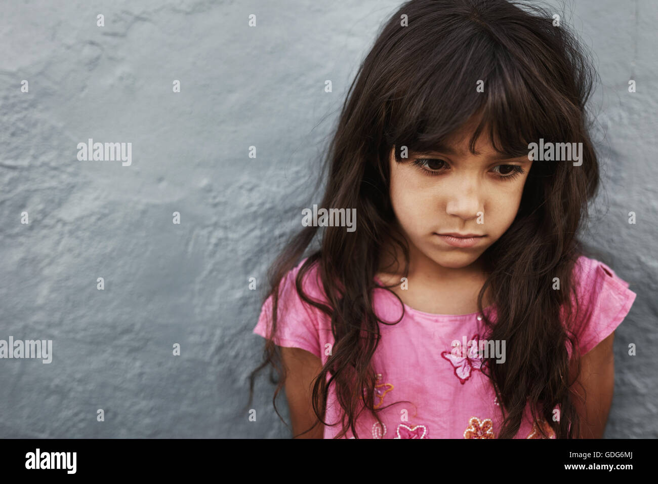 Close up ritratto della infelice bambina in piedi contro il muro grigio con copia spazio. Ragazza giovane cerca sconvolto. Foto Stock