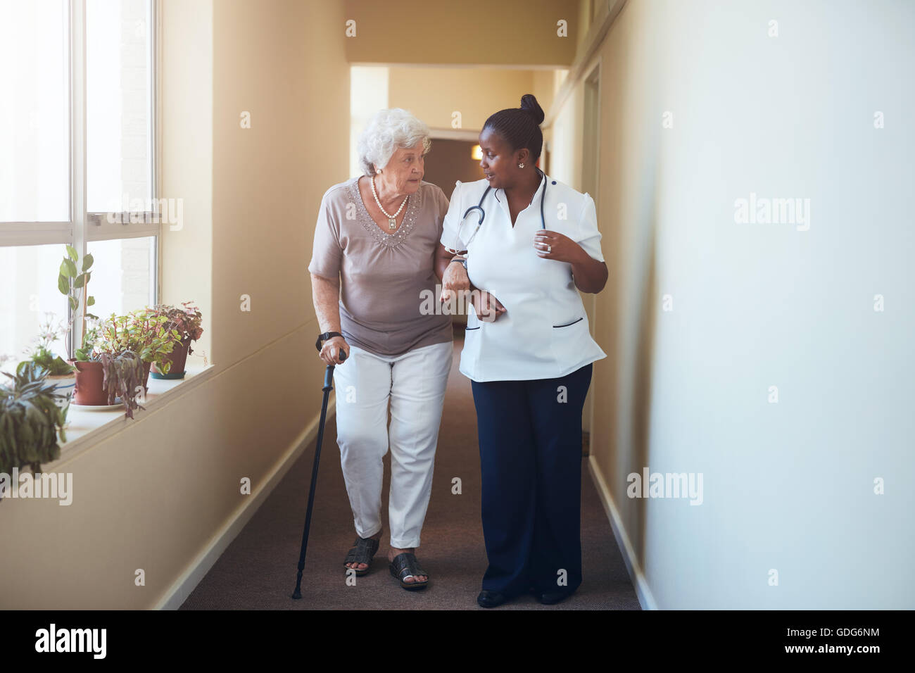 Senior donna con bastone di essere aiutato da un infermiere femmina a casa. A piena lunghezza shot del medico donna con paziente anziano un Foto Stock