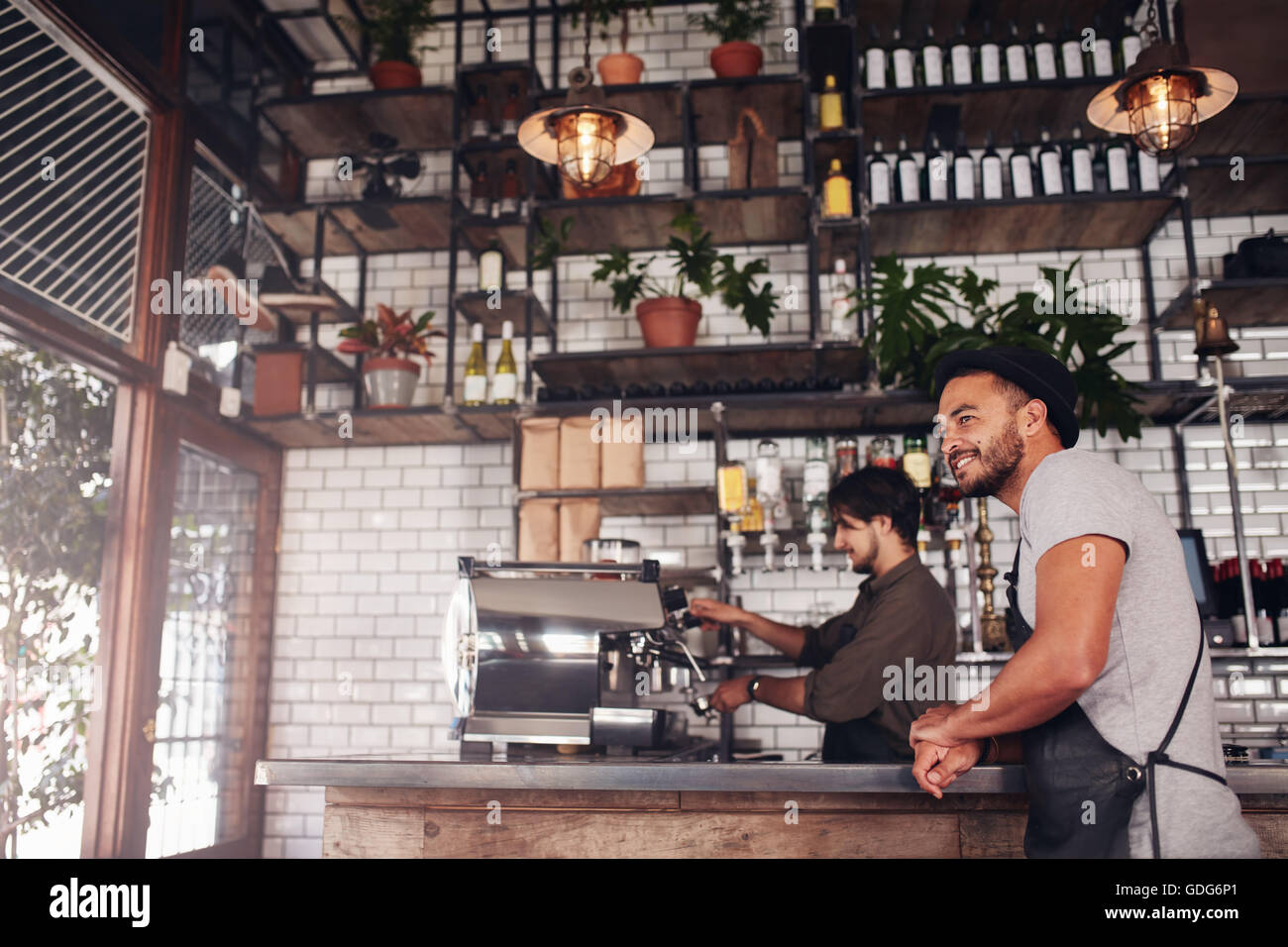 Coffee shop proprietario permanente al contatore, con barista lavora in background. Foto Stock
