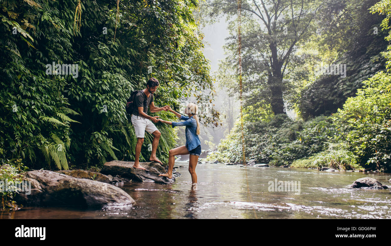 Giovane all'aperto sulla passeggiata con uomo donna assistenza attraverso flusso. Coppia giovane nella foresta che attraversa il torrente. Foto Stock
