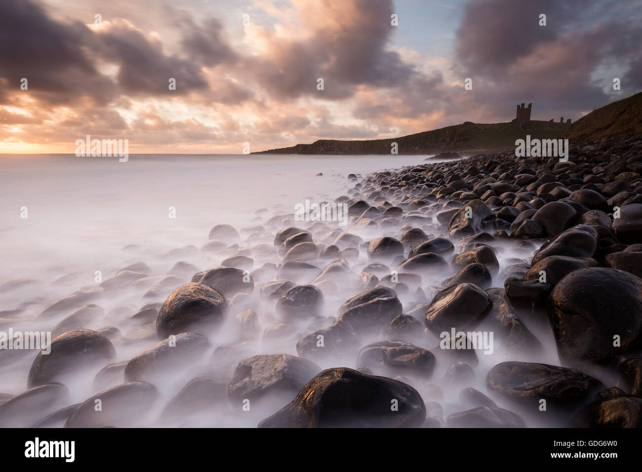 Il mare in tempesta a Embleton Bay con Dunstanburgh castello arroccato sulla scogliera al di là, Northumberland Foto Stock