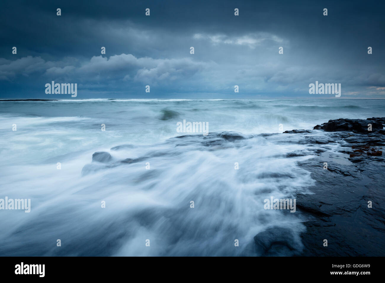 Grandi onde crash sulle rive vicino Craster con un fronte di pioggia sul mare Foto Stock