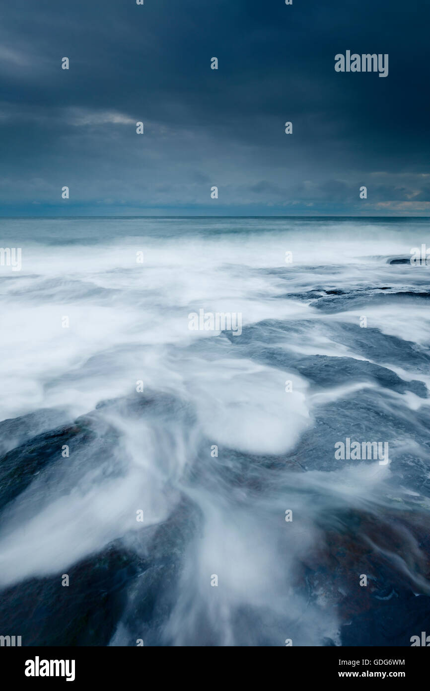 Receding onde su una burrascosa serata vicino Craster Foto Stock