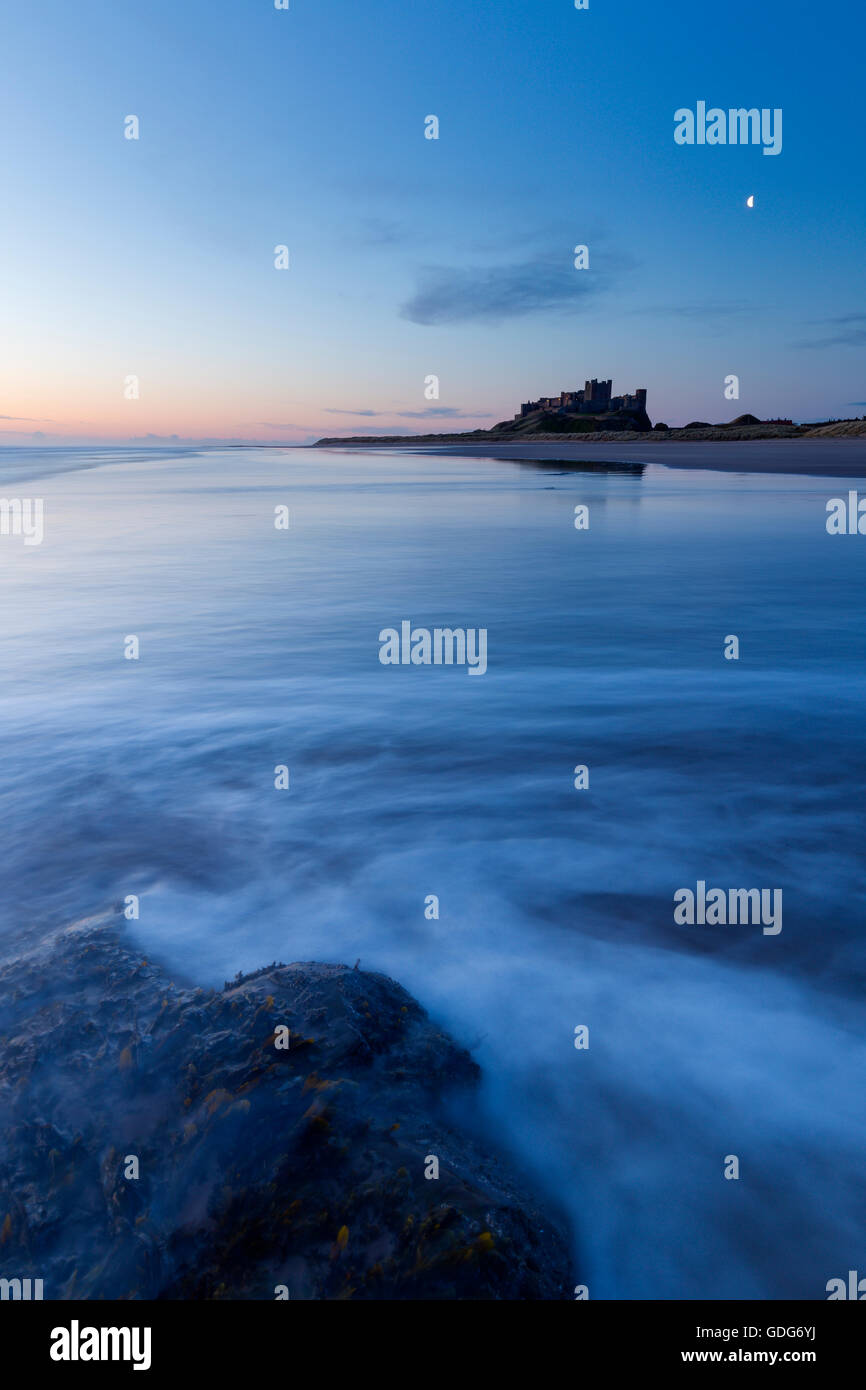 Una luna oltre il castello di Bamburgh all'alba Foto Stock