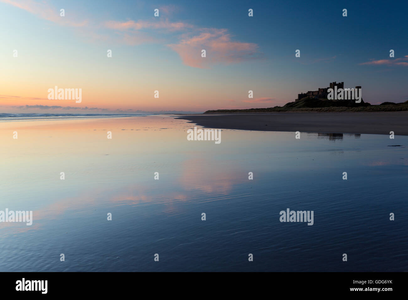 Tenui toni pastle nel cielo sopra il castello di Bamburgh, riflessa sulla spiaggia bagnata, Northumberland, Inghilterra Foto Stock