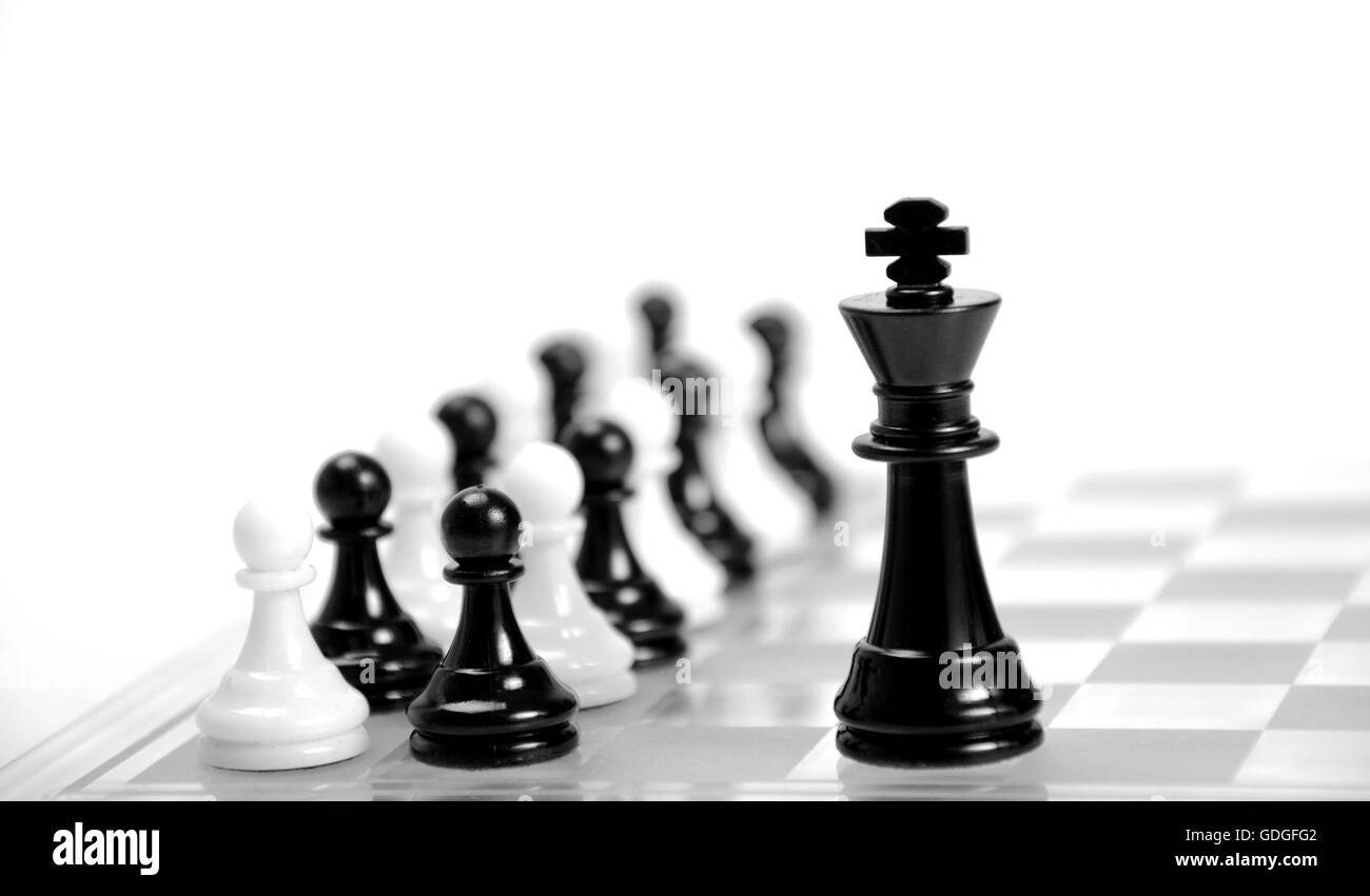 Il bianco e il re nero sulla scacchiera opposti l'uno all'altro,in bianco e nero di pedine in background. Foto Stock