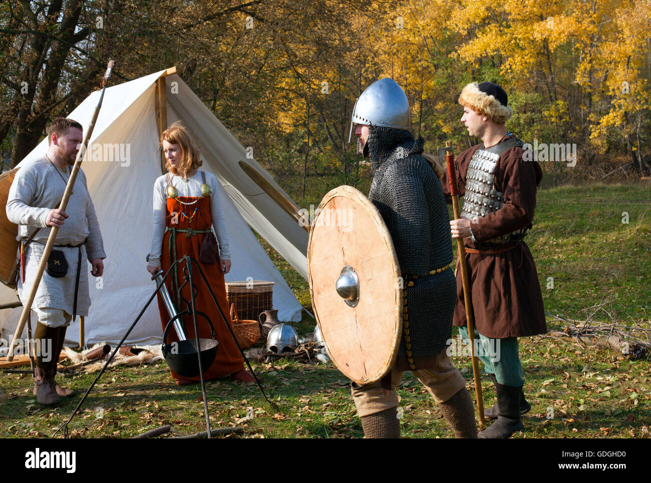 La ricostruzione della vecchia russo vita medievale. Una donna con spada e tre uomini con armi medievali soggiornare vicino tenda bianca. Foto Stock