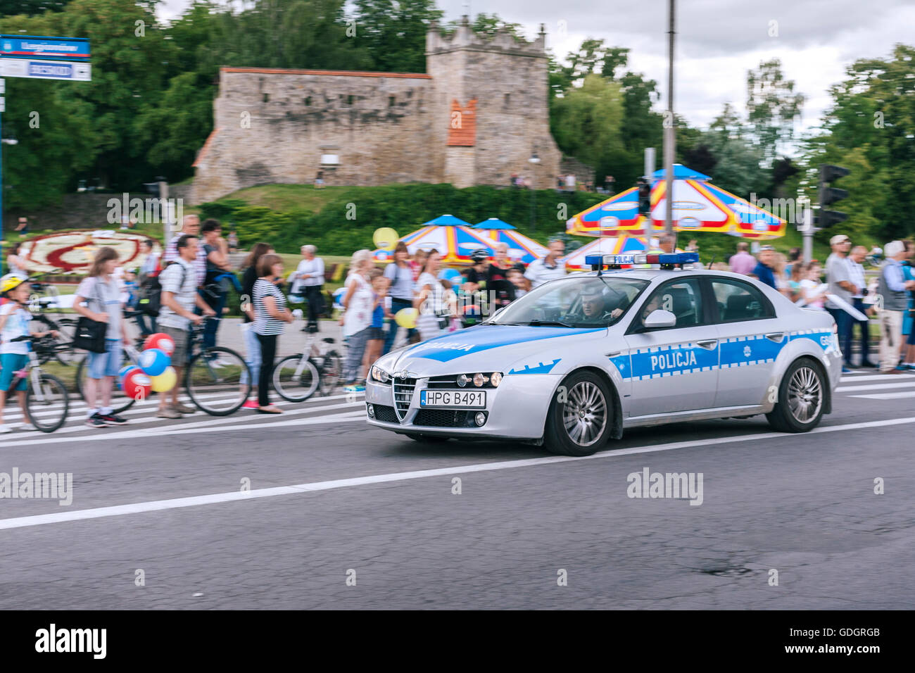 Polish auto della polizia velocizzando il passato per guardare la gente la sfilata con le rovine del castello in background Foto Stock