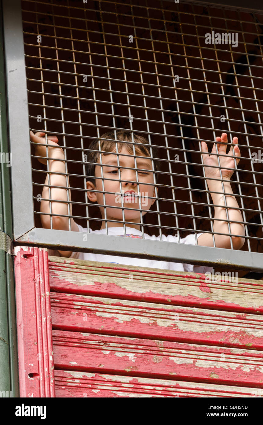 Un bambino guarda attraverso la griglia nella parte superiore di un telaio di arrampicata in un parco giochi per bambini. Foto Stock