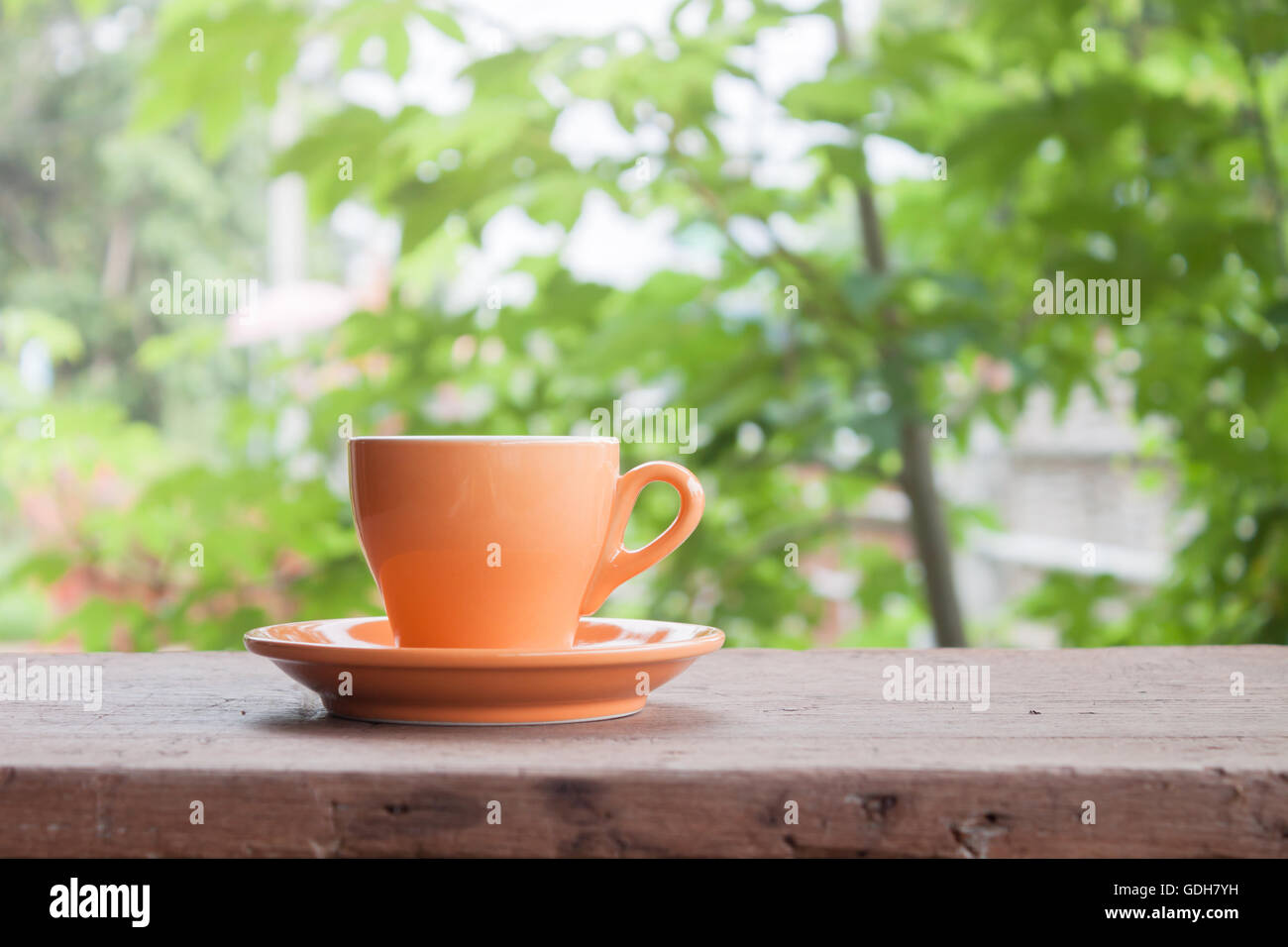 Orange tazza da caffè sul piano portapaziente con sfocate foglie verde sullo sfondo Foto Stock