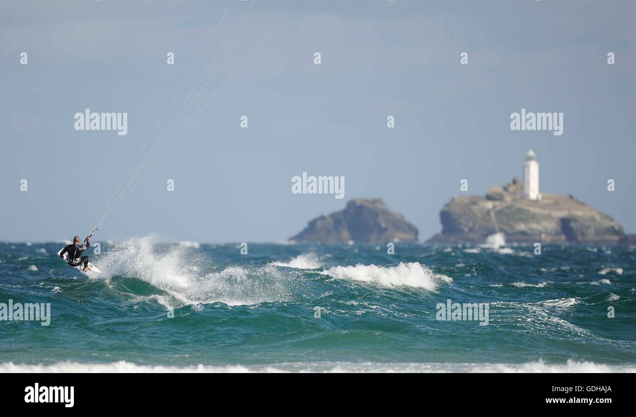 Kite surfer carving off una onda gettando sea spray in aria con Godrevy Lighthouse in background Foto Stock