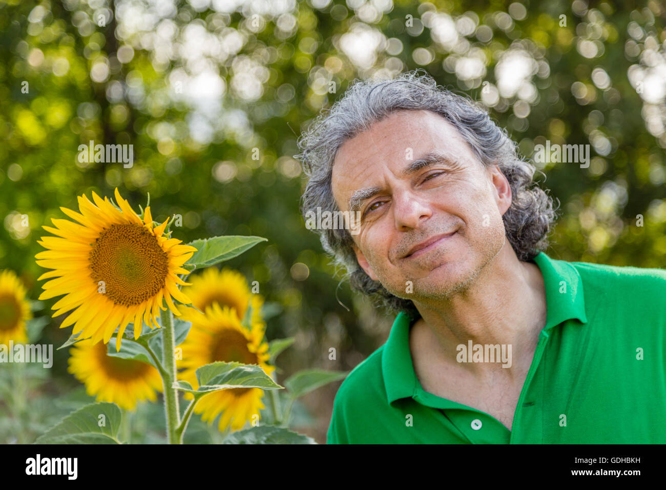 Uomo maturo è sorridente winking accanto di girasoli nella campagna, la natura e la vita all'aperto fargli sentire felice e spensierato Foto Stock