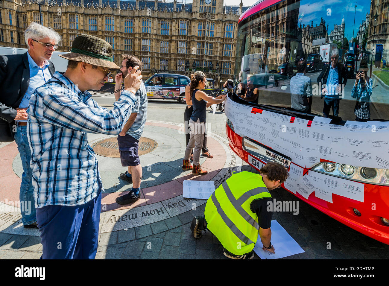 Londra, Regno Unito. 18 Luglio, 2016. John Sauven, direttore esecutivo di Greenpeace UK, orologi come la parte anteriore del bus è coperto in messaggi e un turista prende a scatto - La Brexit 'voto lasciare' battaglia bus (utilizzato da Boris Johnson) è stata acquisita da Greenpeace è stato ri-branded al di fuori del Parlamento. Il £350m NHS rivendicazione è stata coperta con migliaia di domande per il nuovo governo da lasciare e rimanere elettori - molti di loro cosa Brexit mezzi per l'ambiente. Le domande scritte su adesivi, stanno formando un montaggio che illustrerà le parole 'tempo di verità" in grandi lettere bianche sul lato Foto Stock
