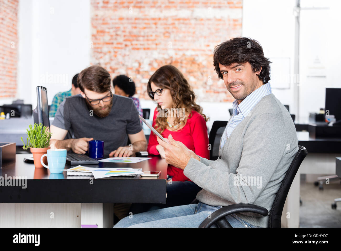 Uomo informale utilizzando tablet seduta lavorando scrivania da ufficio, la gente di affari Foto Stock