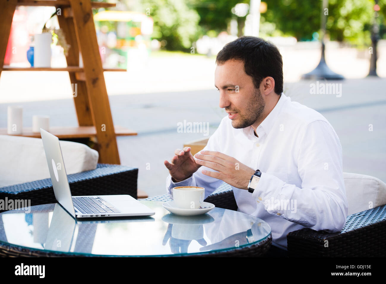 Il lavoro e il relax. Conferenza online. Imprenditore vestito in camicia a lavorare con il computer portatile, parlando da Skype al Park Cafè all'aperto Foto Stock