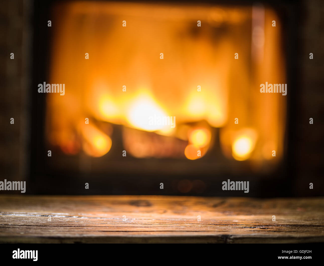 Vecchio tavolo in legno e camino con fuoco caldo sullo sfondo. Foto Stock