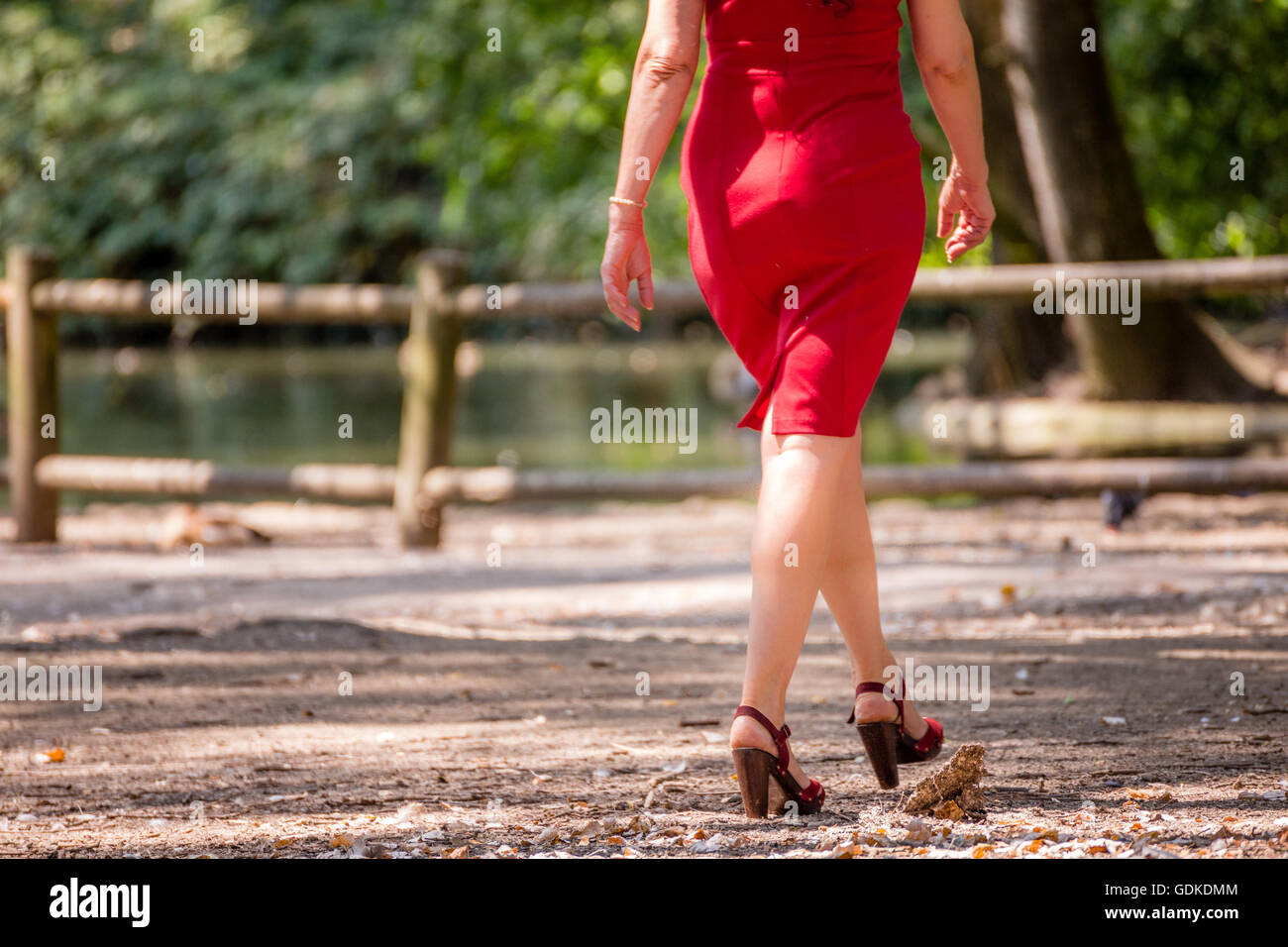Lunga e torniti di donna bendata in matita rossa dress passeggiate nel parco in alta sandali con tacco Foto Stock