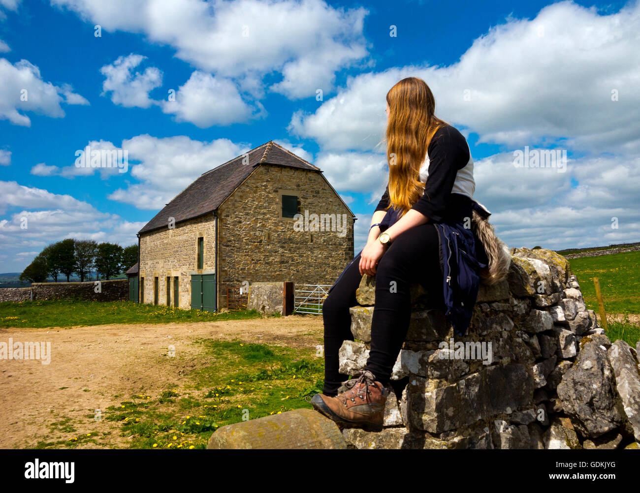 Ragazza seduta su una stalattite parete vicino ad un fienile su un paese a piedi nel Parco Nazionale di Peak District Derbyshire England Regno Unito Foto Stock