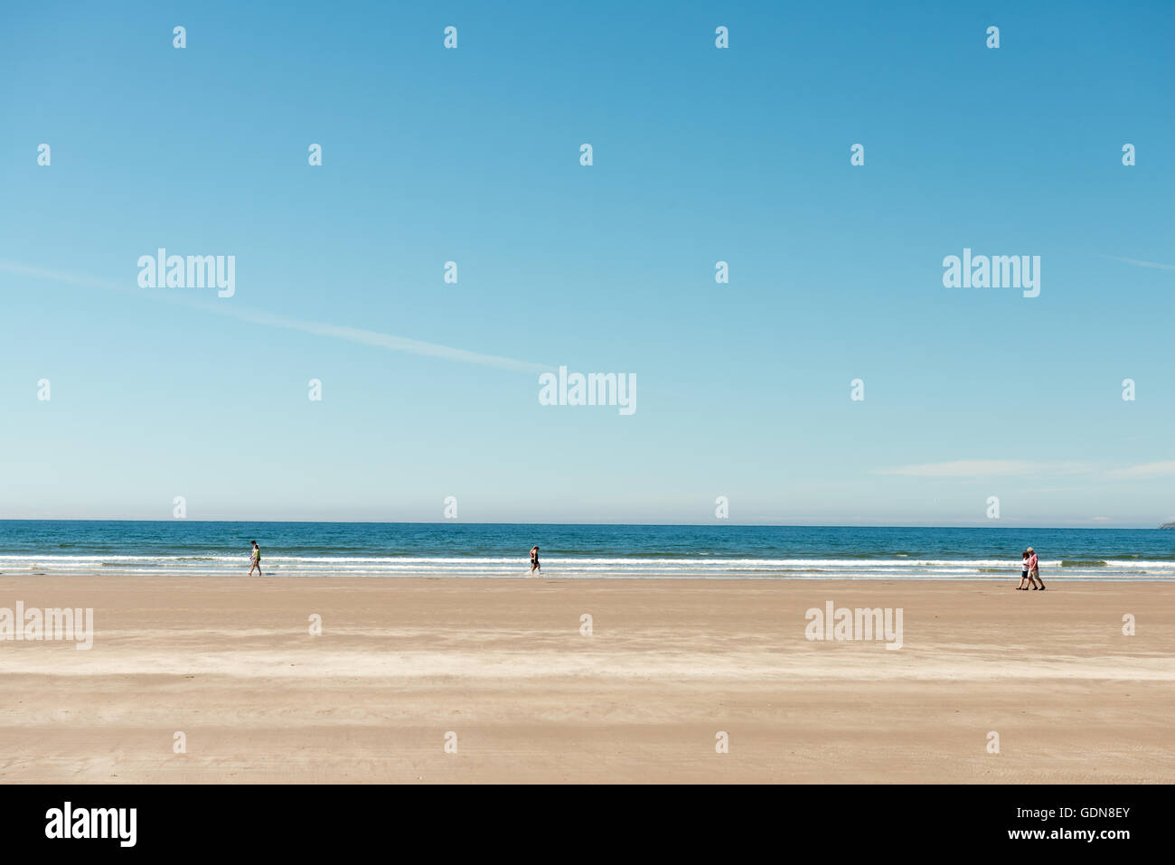 Clima soleggiato: L'Irlanda coppie che camminano sulla spiaggia sabbiosa in una luminosa giornata estiva al largo di Inch Strand, nella contea di Kerry, Irlanda Foto Stock