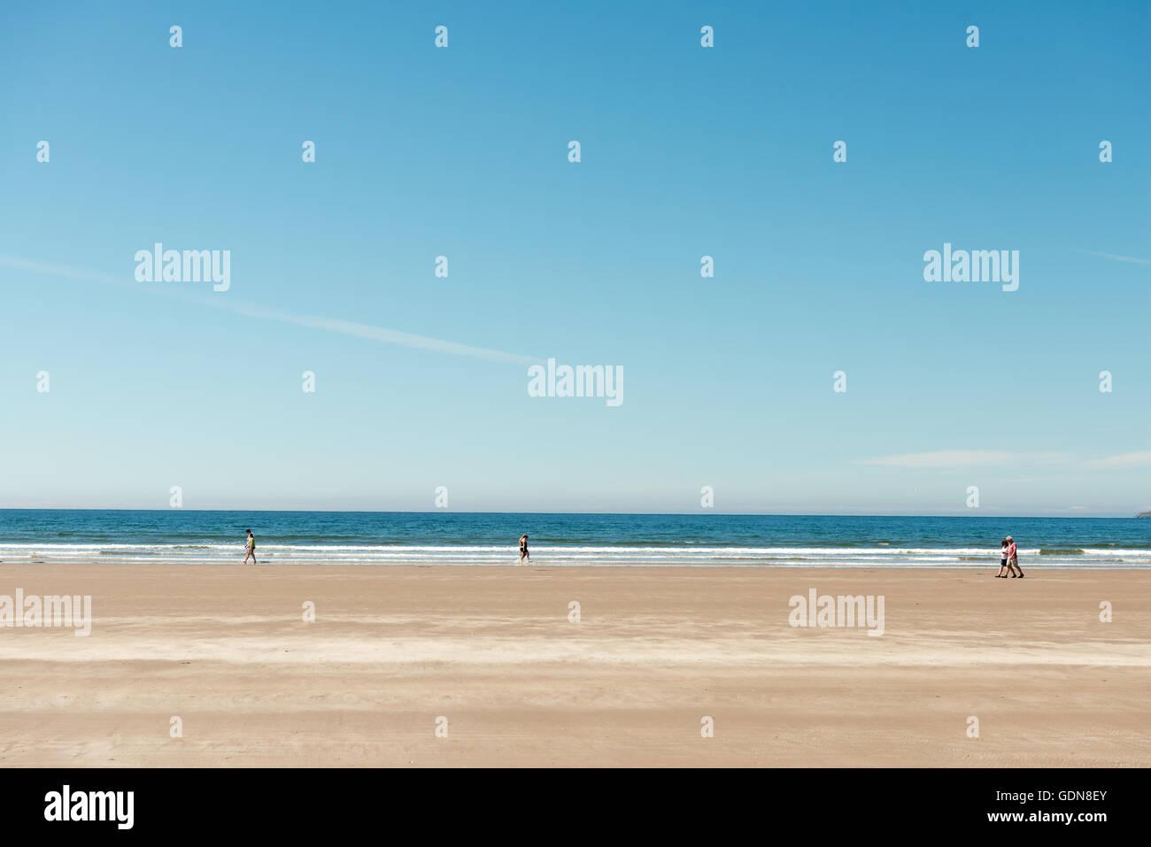 Tre coppie di persone che camminano sulla spiaggia di sabbia in un giorno estivo luminoso e soleggiato all'Inch Strand, County Kerry, Irlanda Foto Stock