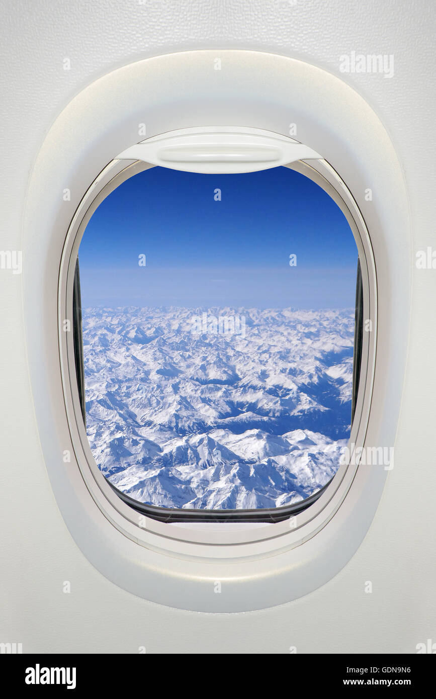 Finestra di un aeroplano dall'interno, vista sulle montagne innevate (Alpi) Foto Stock